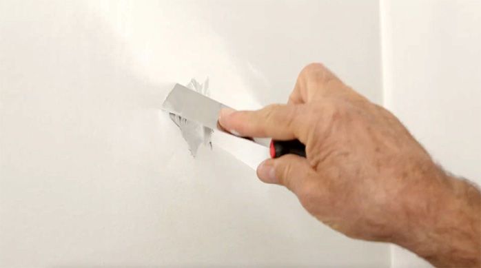 una persona tapa imperfecciones en las paredes del baño de visitas con pasta muro y una espátula