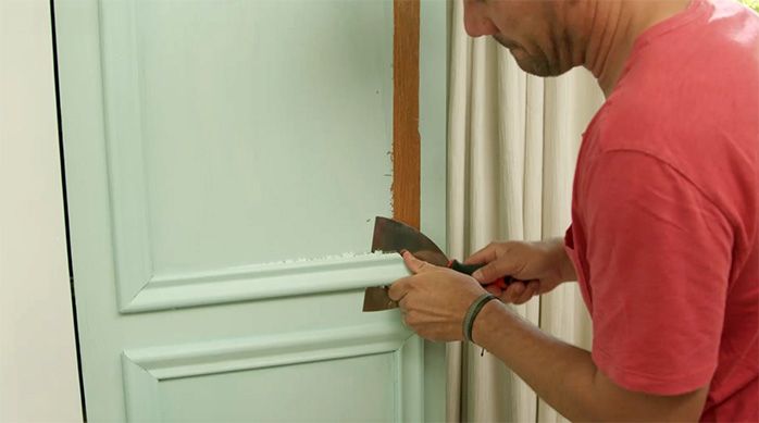 un hombre utiliza una espátula para retirar molduras de una puerta