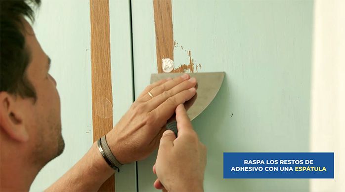 un hombre usa una espátula para raspar restos de adhesivo