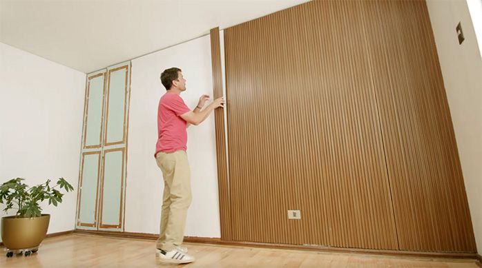 un hombre pega un panel de revestimiento ranurado en un muro interior