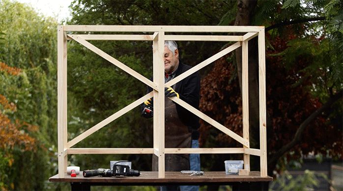 un hombre fija 2 diagonales en la parte posterior de la estructura de madera