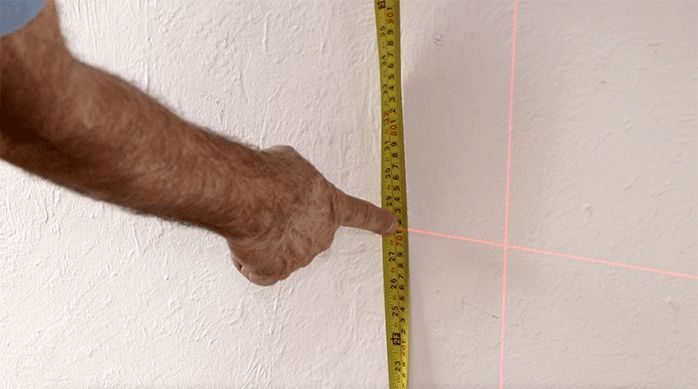 un hombre apunta con el dedo una huincha de medir que está siendo comparada con un nivel láser