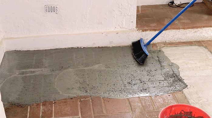una persona esparce la lechada con un escobillón en el piso del comedor para pegar porcelanato para piso