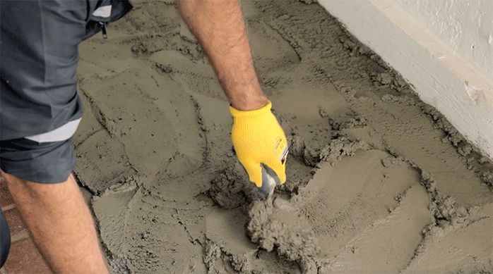 una persona esparce el nivelador para pisos topex con una plana