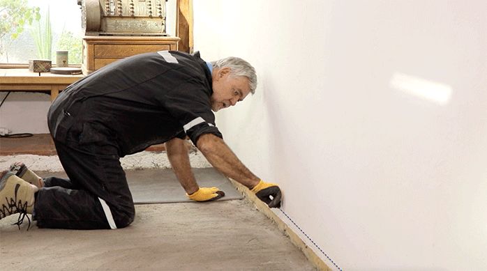 una persona usa un tizador para hacer una línea guía para poner las planchas de porcelanato para piso