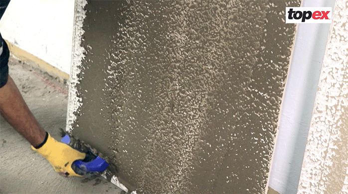 un hombre pone pegamento para porcelanato para piso con una llana en la parte de atrás de una plancha de porcelanato de gran formato