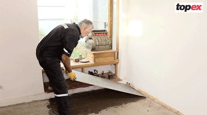 un hombre pega una plancha de porcelanato para piso en el piso de un comedor