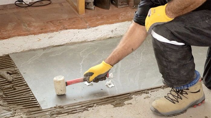 un hombre golpea con un martillo de goma la plancha de porcelanato para piso para que se asiente