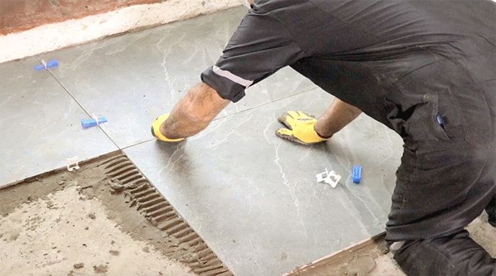 un hombre pone separadores y cuñas niveladoras entre las planchas de porcelanato para piso