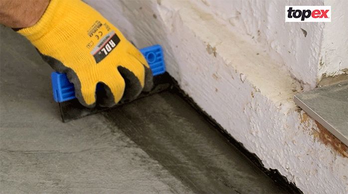 una persona aplica el fragüe en el porcelanato para piso con una lengüeta de goma