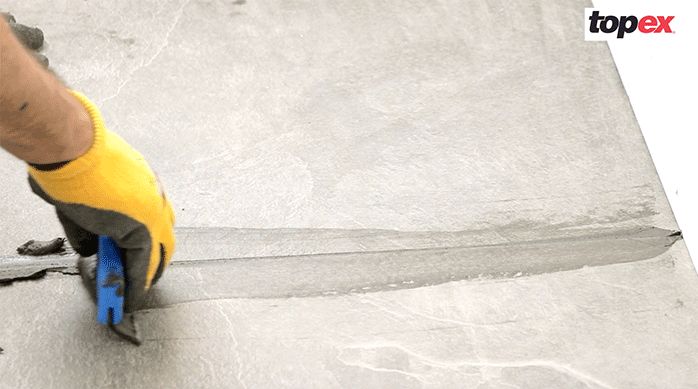 una persona pasa una lengüeta de goma para esparcir bien el fragüe en el porcelanato para piso
