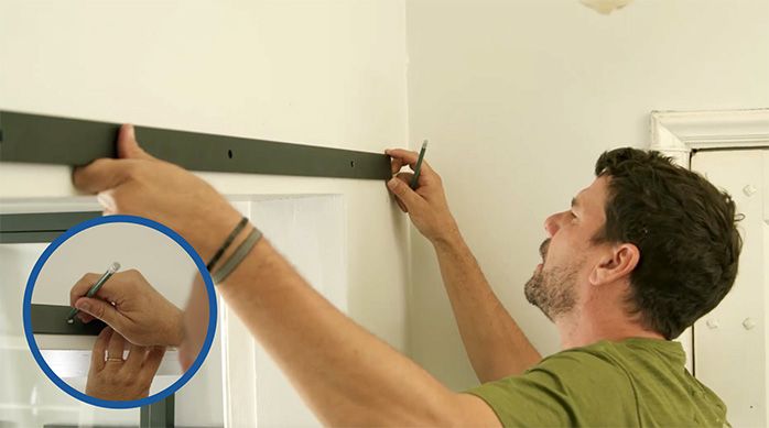 un hombre presenta el riel para puerta corredera interior en el muro y marca a través de sus agujeros