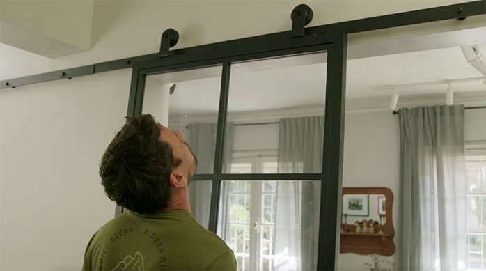 un hombre pone la puerta corredera interior con sus dos ruedas en el riel para puerta corredera