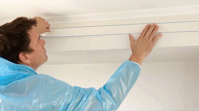 un hombre pone cinta para enmascarar en la parte superior del muro de una habitación