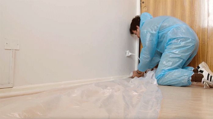 un hombre pone un cobertor plástico para proteger el piso y pintar el cielo