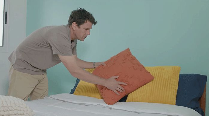 un hombre pone cojines decorativos en la cama