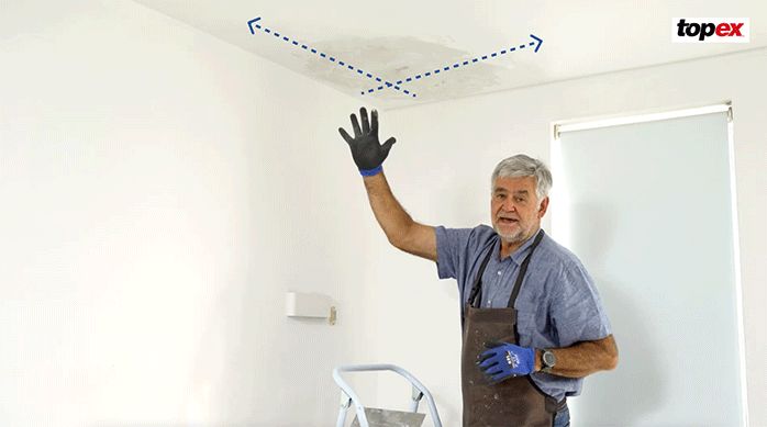un hombre muestra cómo poner pasta muro en diferentes direcciones para reparar un cielo raso con humedad