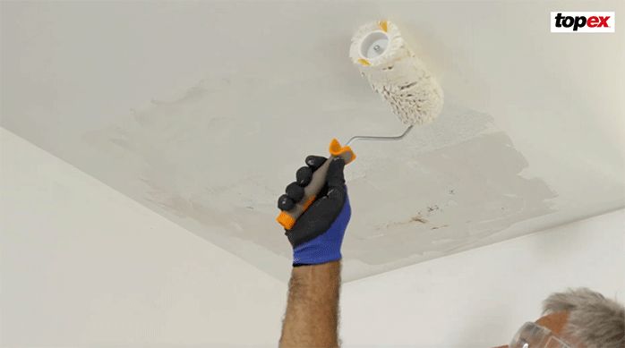 un hombre usa un rodillo anti gota para aplicar pintura látex en el cielo raso