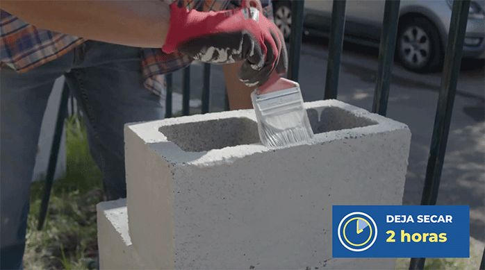 un hombre pinta la estructura de ladrillos de concreto con una brocha y pintura antihongos