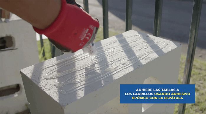 un hombre aplica adhesivo epóxico en la estructura de ladrillos para pegar la banca de madera