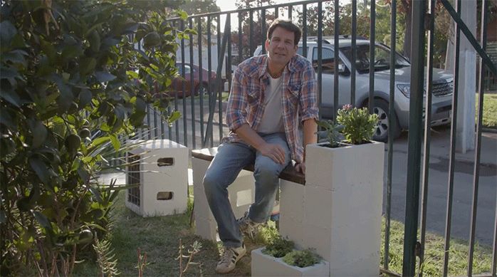 un hombre sentado en una banca de madera que oculta el medidor de agua en un antejardín