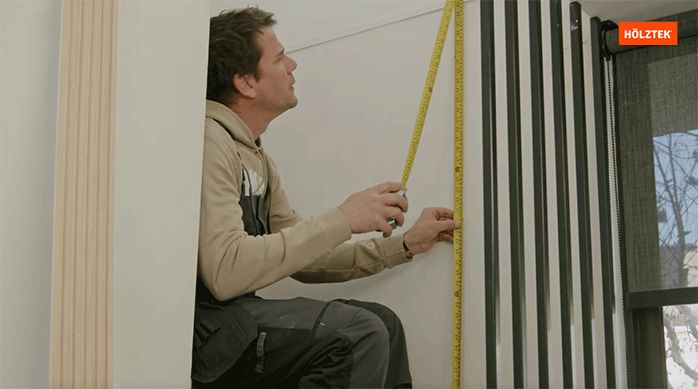 un hombre mide con una huincha el alto del muro de una escalera para instalar revestimiento ranurado.