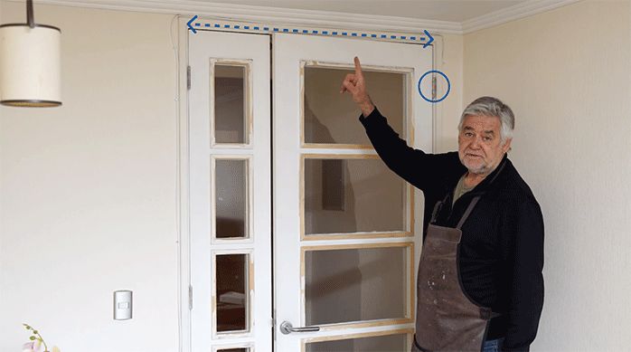 un hombre muestra una puerta que no cierra bien, ya que tiene bisagras deformadas y topa con la parte superior del marco.