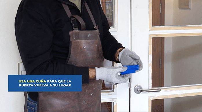 un hombre sostiene y muestra 2 cuñas niveladoras para arreglar una puerta.