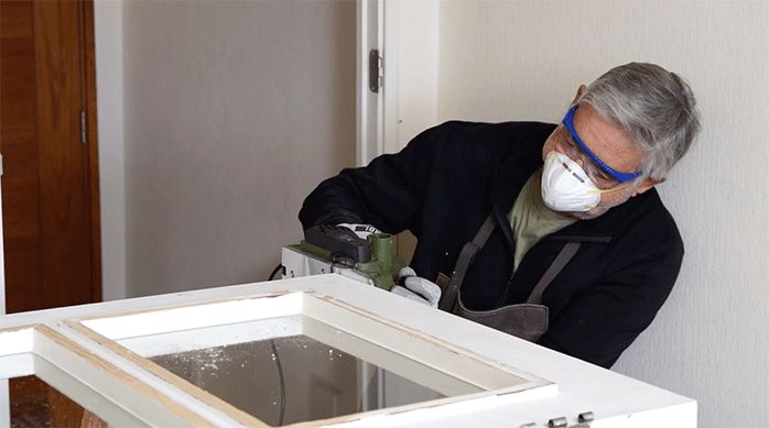 un hombre rebaja una puerta con un cepillo eléctrico.