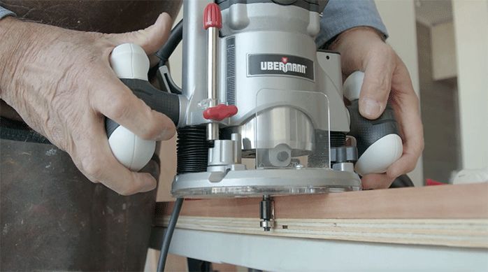 un hombre usa una fresadora con una fresa copiadora para rebajar las tablas de roble vaporizado para armar el mueble de arrimo para sofá.