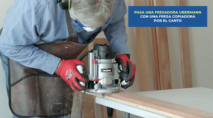 un hombre pasa la fresadora con una fresa copiadora por el borde de las tablas de roble vaporizado.