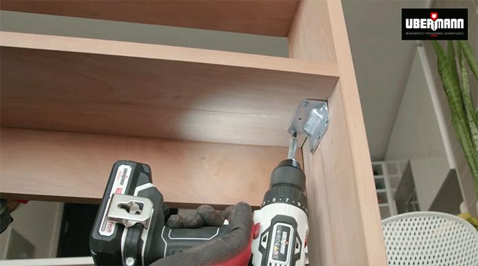 un hombre fija la repisa inferior del mueble de arrimo a la escuadra de aluminio.