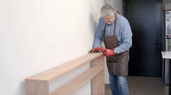 un hombre lija el mueble de arrimo con una lija puesta en un soporte manual.