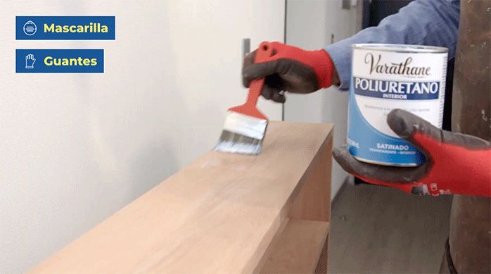 un hombre aplica barniz poliuretano con una brocha en el mueble de arrimo para sofá.