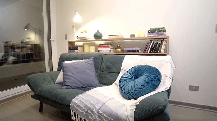 un sofá con un mueble de arrimo para libros en la parte posterior, con libros y lámpara.