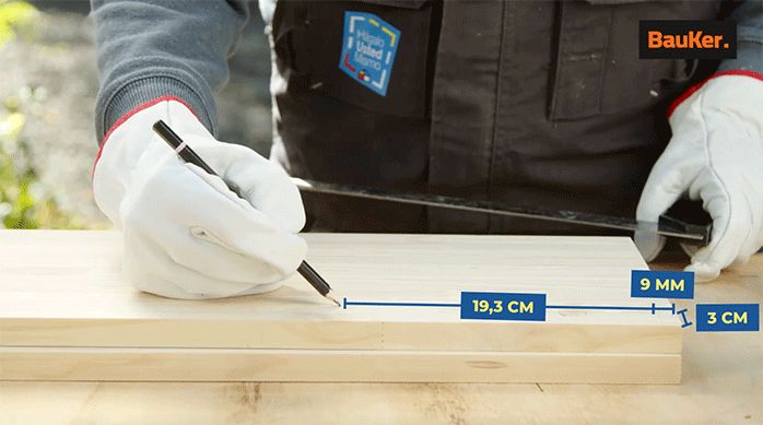 un hombre marca las perforaciones en un trozo de madera laminada para crear un mueble organizador para baño.
