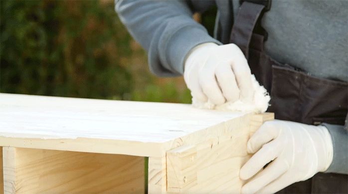 un hombre aplica impregnante o stein con un huaipe en los muebles organizadores para lavamanos.