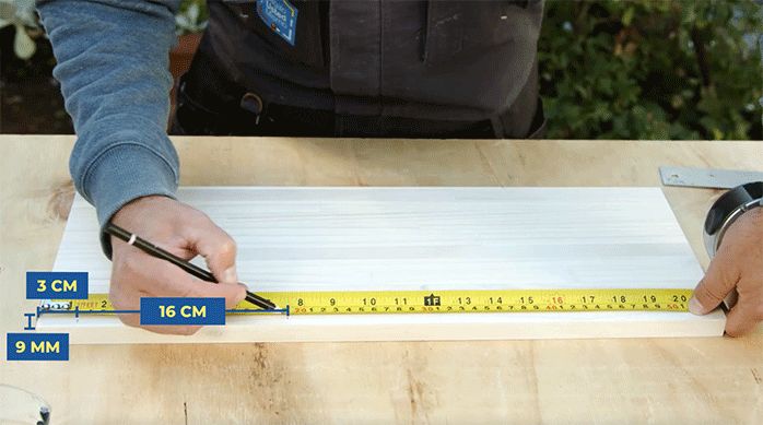 un hombre marca en un trozo de madera laminada las perforaciones necesarias para hacer una repisa en el baño.
