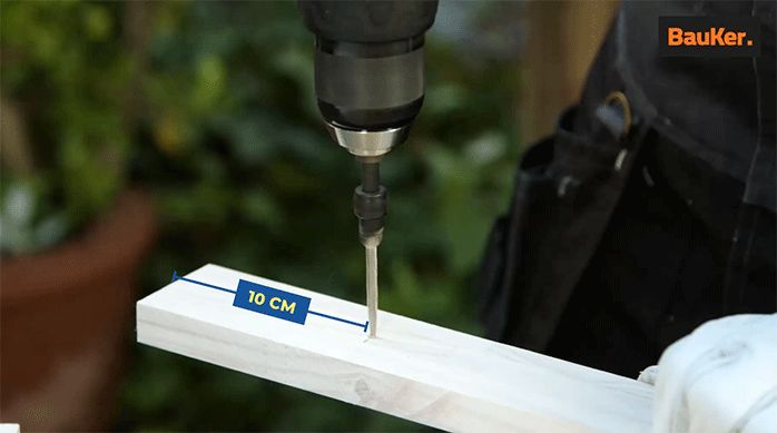 un hombre perfora un trozo de madera laminada a 10 cm del extremo.