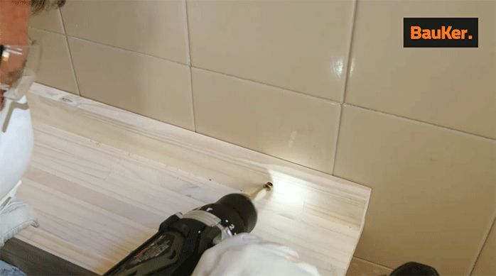 un hombre fija la repisa de madera laminada en el muro del baño.