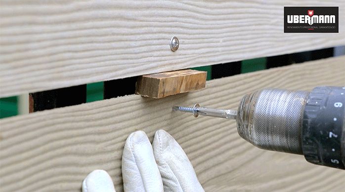 un hombre instala siding de fibrocemento en una reja usando una guía de separación entre las tablas.