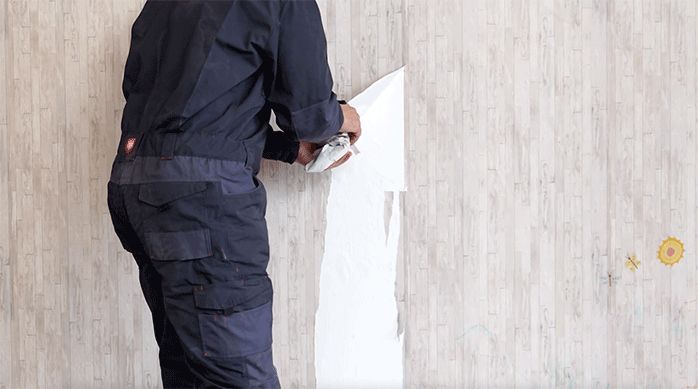 un hombre saca papel mural en pedazos grandes con la mano.