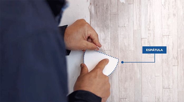 un hombre saca papel mural fácilmente con una espátula luego de humedecerlo.