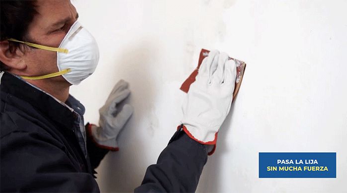 un hombre pasa una lija en el sector con pegamento en un muro.