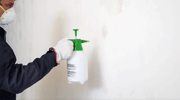 un hombre vuelve a humedecer la pared con un pulverizador para retirar el pegamento.