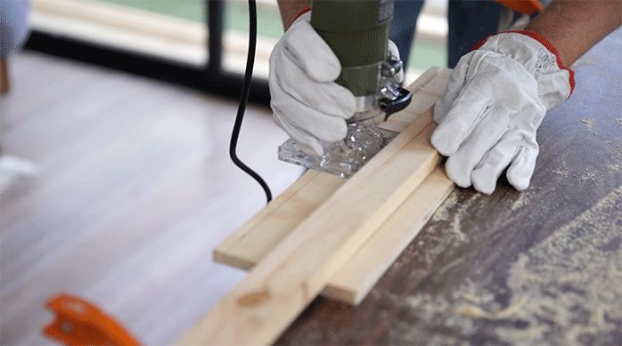 un hombre usa una fresadora para hacer un surco en los trozos de madera para hacer el cajón del mueble.