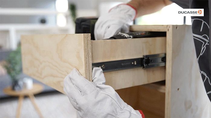 un hombre fija la tapa delantera del mueble en la cara frontal del cajón.