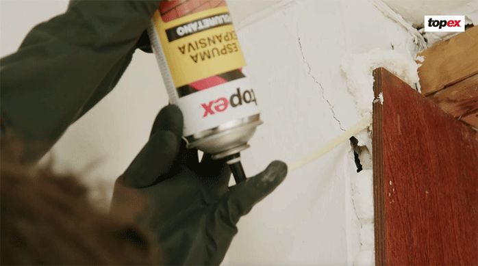 un hombre aplica espuma de poliuretano en una grieta en el muro.