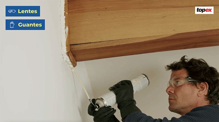 un hombre rellena una grieta en el cielo de una habitación con espuma de poliuretano para paredes.