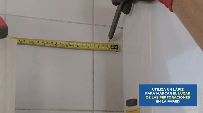 un hombre marca un lugar de fijación en el muro de la cocina al lado del cálefont.